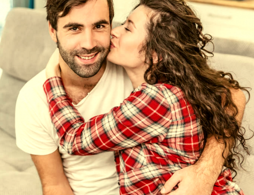 Happy couple sitting on couce as she kisses his cheeck from blog Secrets to Having a Long-lasting Marriage | GreatPeaceLiving.com #marriagemoments #marriage